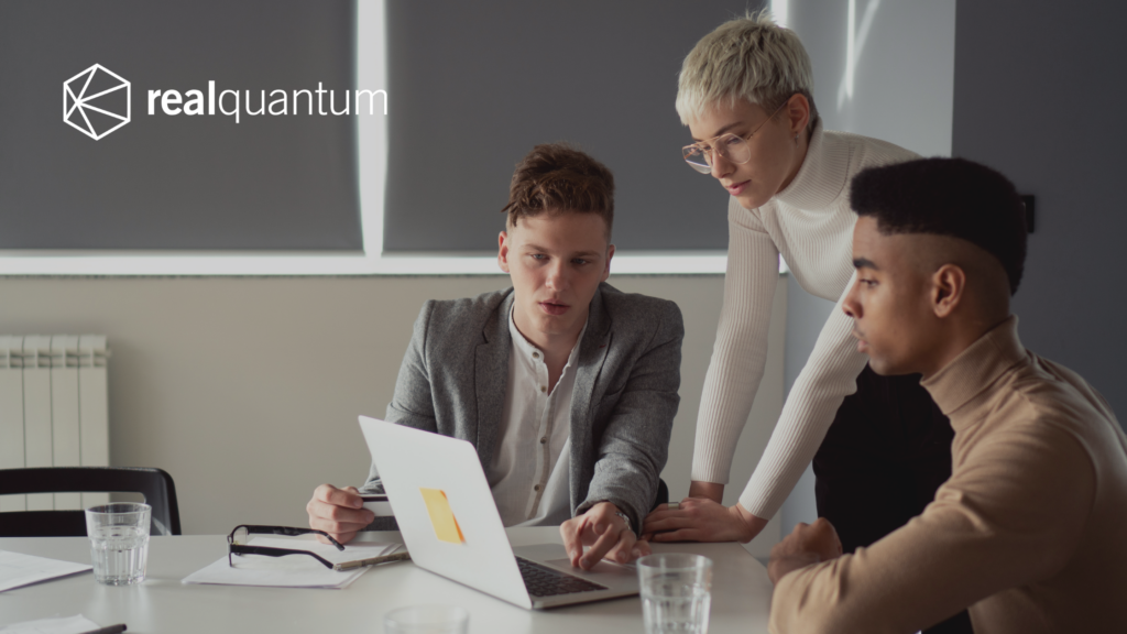 Professionals sit around the table looking at the laptop screen.